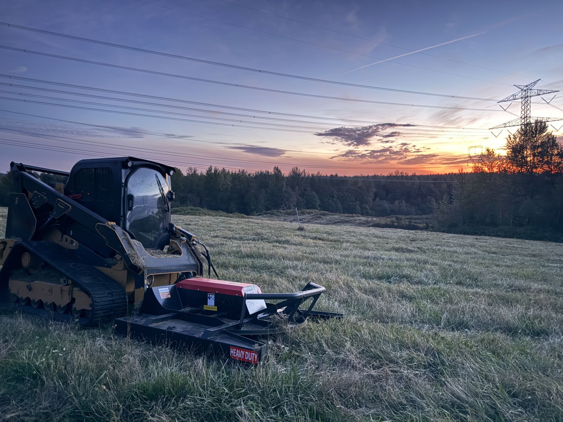 Compact track loader with brush cutter at sunset